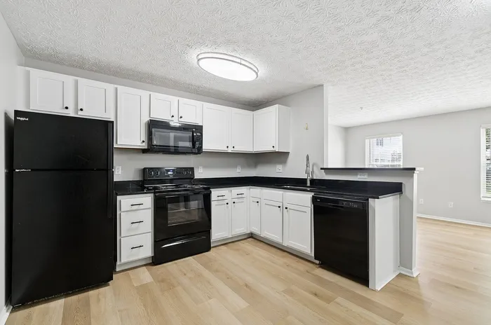 Modern kitchen with sleek black appliances, white cabinetry, and hardwood floors, perfect for contemporary living.