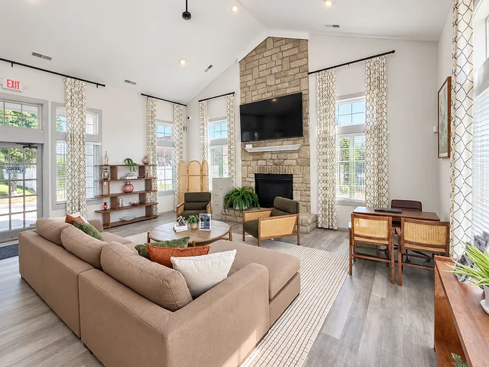 Bright and cozy living room with modern decor, featuring a stone fireplace, large sectional sofa, and expansive windows with elegant drapery.