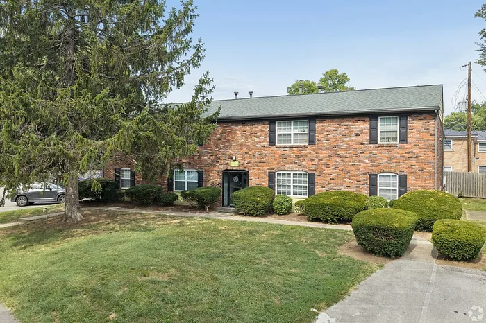Charming brick apartment building with large windows and lush landscaping, offering a serene residential setting.