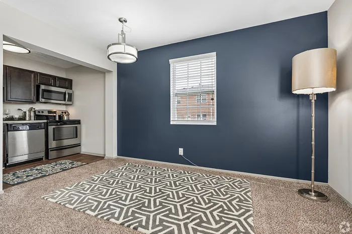 Elegant apartment dining area with plush carpet, modern light fixture, and stainless steel kitchen appliances.