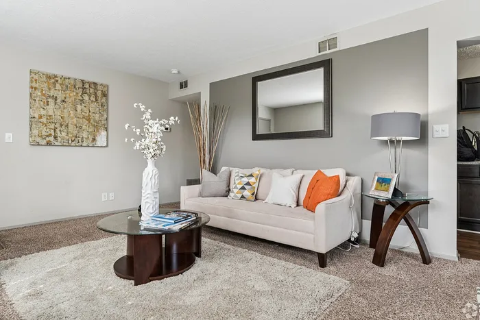 Modern living room with stylish decor, featuring a cozy beige sofa with vibrant cushions, a chic glass coffee table, and elegant wall art.