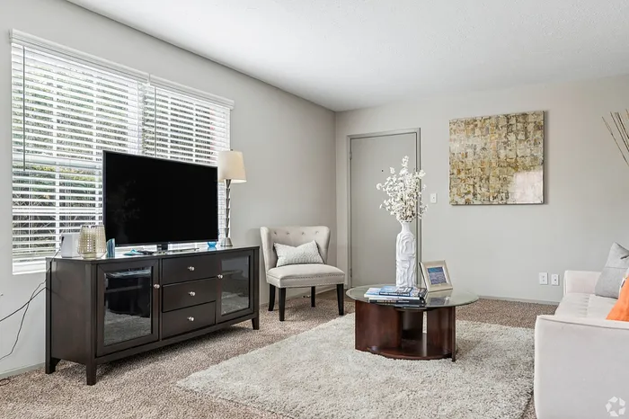 Bright and welcoming living room with modern decor, featuring a sleek TV stand, plush chair, and contemporary artwork, bathed in natural light.