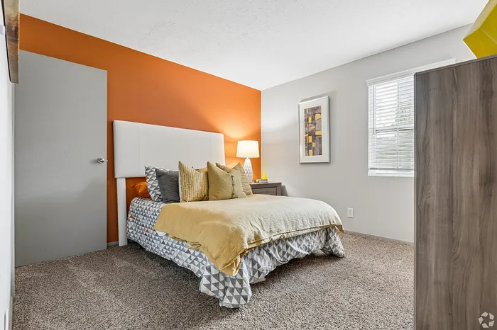 Inviting bedroom with vibrant orange accent wall, stylish bedding, and natural light filtering through the window.