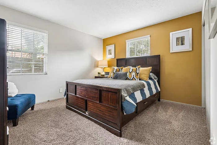 Cozy bedroom with a plush carpet, elegant wood bed frame, and stylish accent wall, flooded with natural light from two large windows.