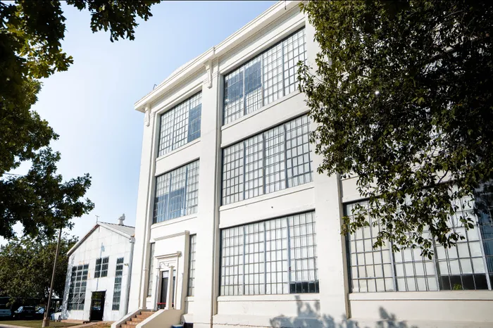 Chic urban industrial-style building with large grid windows surrounded by lush greenery.