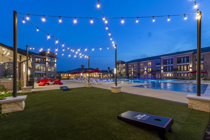 Modern apartment complex with sparkling pool, ambient string lights, and inviting outdoor lounge area set against a twilight sky.