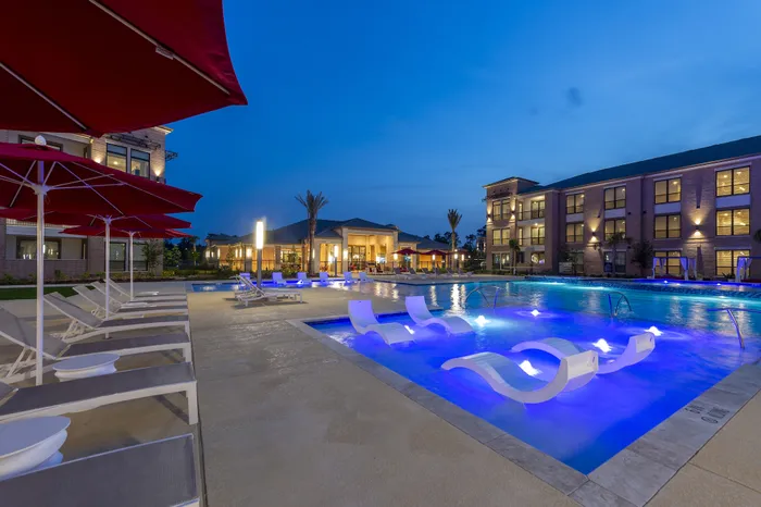 Luxurious apartment community pool at dusk with ambient lighting, elegant lounge chairs, and inviting poolside amenities.