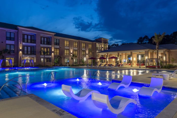 Luxury apartment complex at twilight with a beautifully illuminated swimming pool and stylish poolside seating, surrounded by elegant architecture.