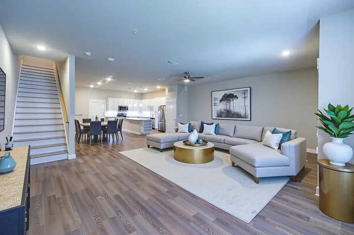 Modern open-concept living room with stylish gray sectional, chic dining area, and sleek kitchen, highlighted by elegant lighting and warm wood floors.
