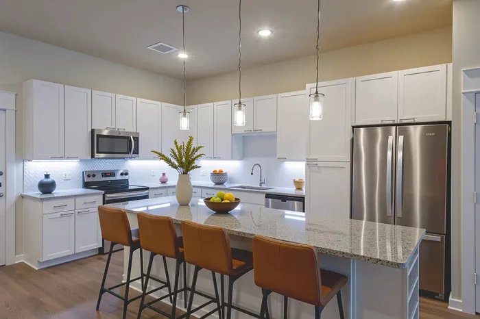 Modern kitchen with sleek stainless steel appliances, elegant white cabinetry, and a spacious granite island with bar seating; warm lighting enhances the contemporary design.