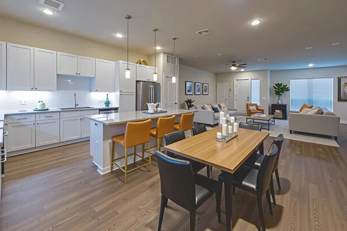 Modern open-concept kitchen and living area featuring sleek white cabinetry, a spacious island with stylish bar seating, and elegant dining space, perfect for entertaining.