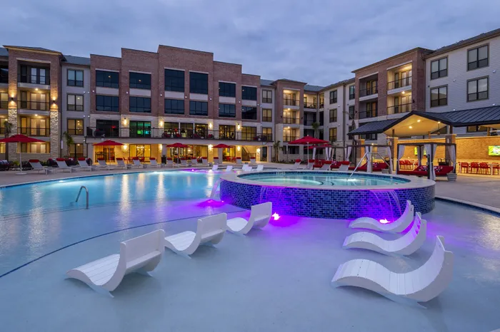 Luxurious apartment complex with illuminated pool and stylish outdoor lounge area, perfect for relaxation and social gatherings.