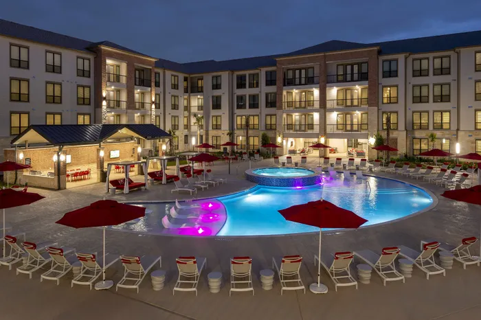Luxurious apartment complex featuring a stunning illuminated pool area with elegant red umbrellas and cozy cabanas.