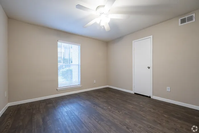 Inviting bedroom with elegant wood flooring, large window providing natural light, and ceiling fan for comfortable living.