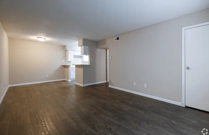 Spacious apartment living area with elegant wood flooring and open-access kitchen, perfect for modern living.