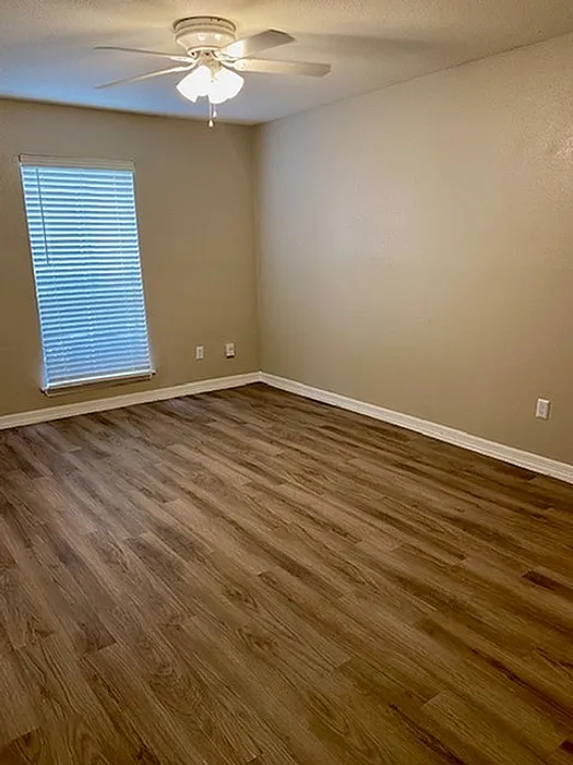 Inviting bedroom with elegant wood flooring, soft beige walls, and ample natural light from a large window, ideal for relaxation.