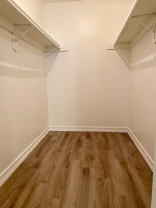 Spacious walk-in closet with elegant wooden flooring and dual shelf storage, offering ample organization space.