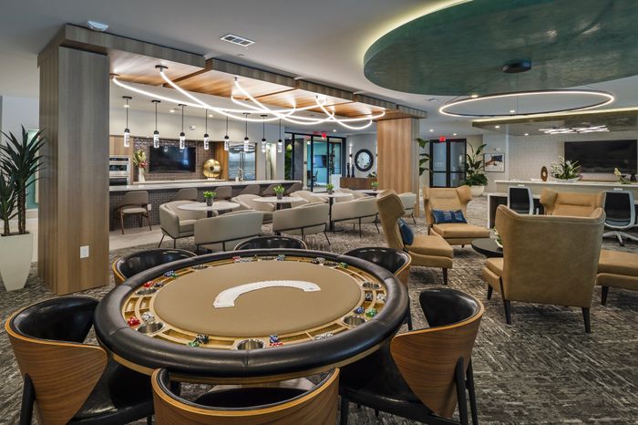 Luxurious apartment lounge with modern decor, featuring a stylish poker table and comfortable seating areas under artistic lighting.