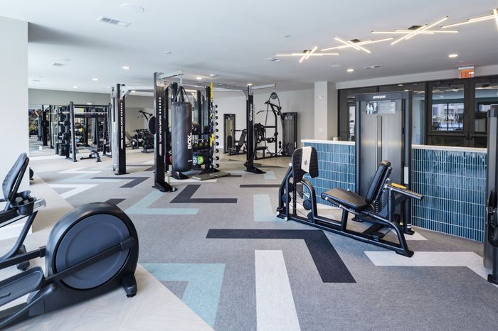 Modern fitness center with state-of-the-art gym equipment and sleek design, featuring cardio machines and weight stations on stylish geometric flooring.