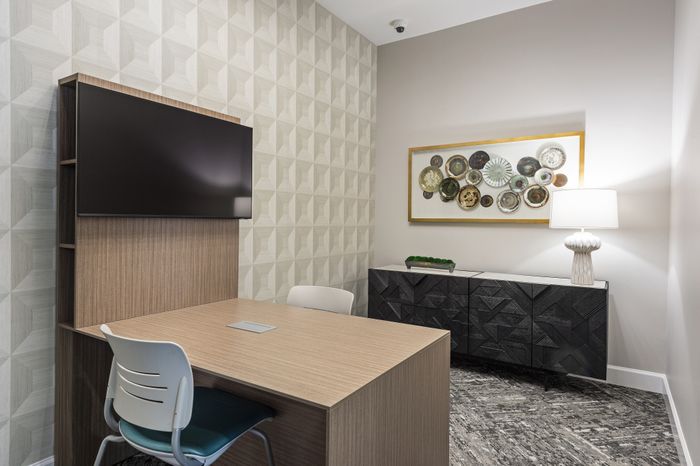 Modern office space with artistic wall decor, featuring a sleek wooden table, contemporary chairs, and a stylish textured cabinet with elegant lighting.