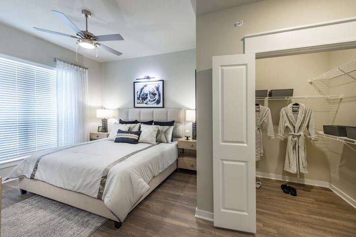 Elegant bedroom featuring a cozy bed with stylish cushions, walk-in closet with plush robes, and modern ceiling fan, bathed in natural light.