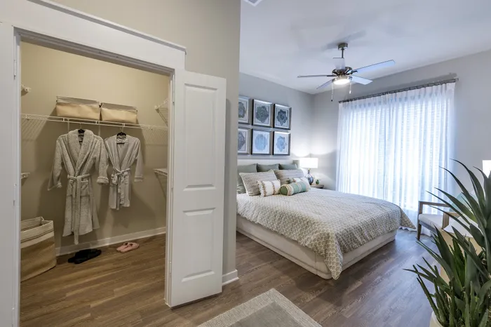 Inviting bedroom with elegant decor, large windows, and an open closet featuring plush robes, ideal for comfort and style.