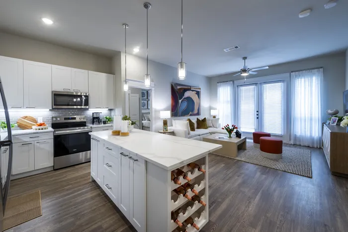 Modern open-plan kitchen and living room with elegant white cabinetry, sleek island, wood flooring, and stylish decor, flooded with natural light.
