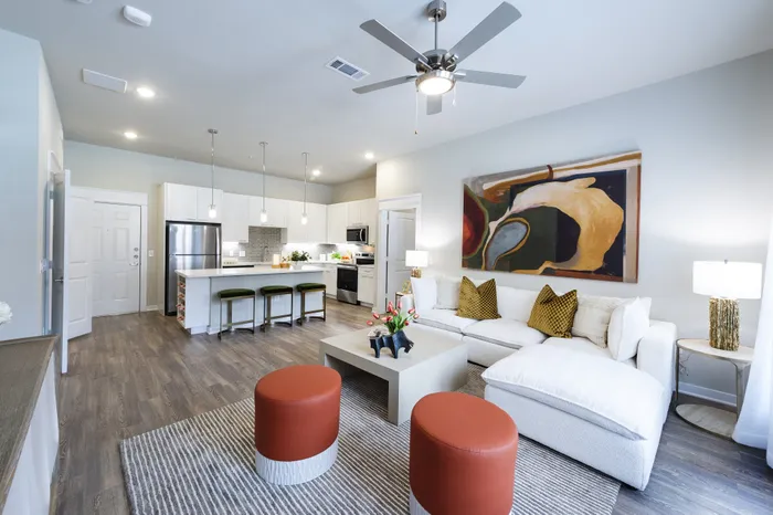 Modern open-concept living room with stylish decor, featuring cozy white sofa, vibrant wall art, and sleek kitchen with breakfast bar.