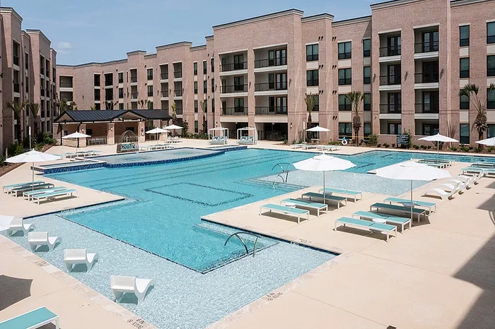 Luxury apartment complex featuring a stunning outdoor pool surrounded by lounge chairs, umbrellas, and modern architecture.