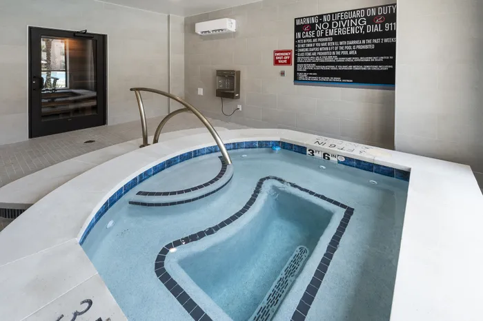 Luxurious indoor hot tub with modern tiling and sleek railing, providing a relaxing retreat in a stylish setting.