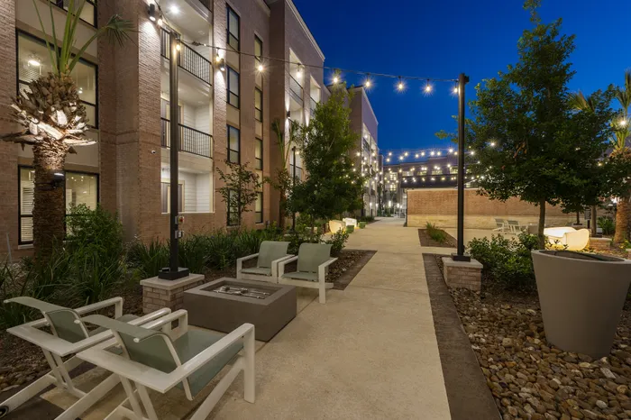 Charming courtyard at night with string lights, lush landscaping, and cozy seating in a modern apartment complex.