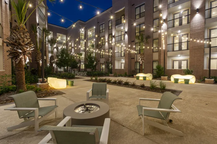 Charming apartment courtyard with cozy seating and twinkling string lights, set against a modern building facade at night.