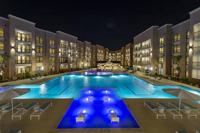 Luxurious apartment complex featuring a stunning illuminated pool at night, with modern amenities and elegant architecture.
