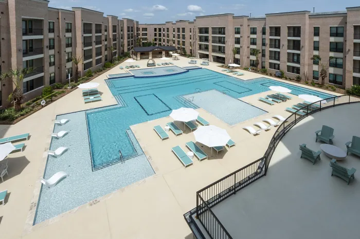 Luxurious apartment complex featuring a stunning outdoor pool area with modern lounge chairs and shaded seating, surrounded by elegant multi-story buildings.