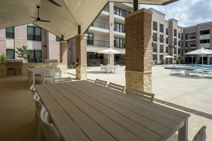 Chic outdoor communal space with dining tables, shaded seating area, and inviting pool view at a modern apartment complex.
