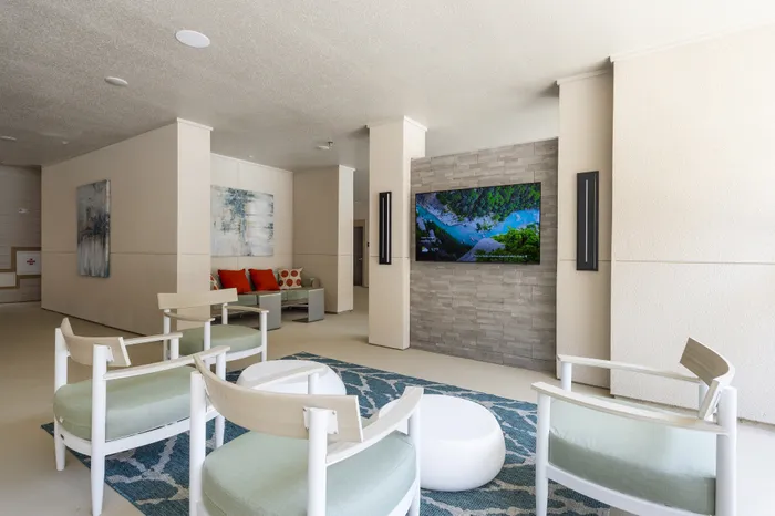 Stylish and modern lounge area featuring elegant seating, a large flat-screen TV on a textured wall, and contemporary artwork for a welcoming ambiance.