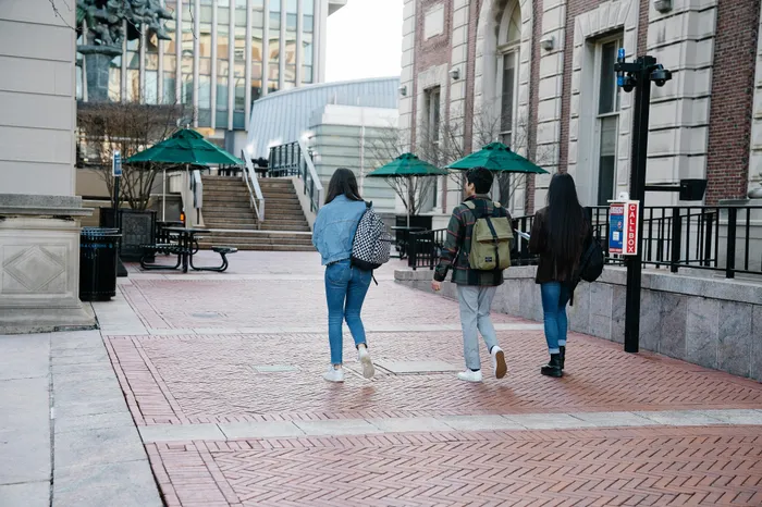 Three people walking through a vibrant urban plaza with stylish brickwork and modern architecture in the background.