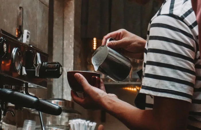 Close-up of a barista skillfully pouring milk into a coffee cup, creating a cozy and inviting coffee shop atmosphere.