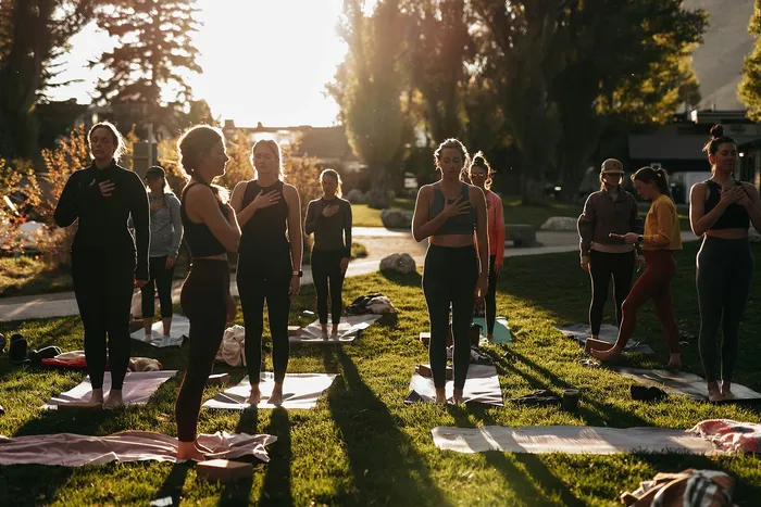 Serene outdoor yoga session at sunset with a group of people practicing mindfulness on mats, surrounded by lush greenery.