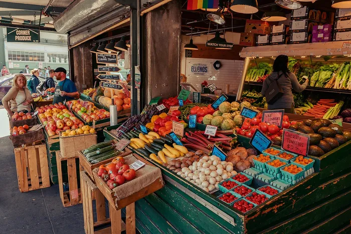 Vibrant outdoor market stall brimming with fresh fruits and vegetables, including apples, avocados, and tomatoes, creating a colorful display and lively shopping atmosphere.