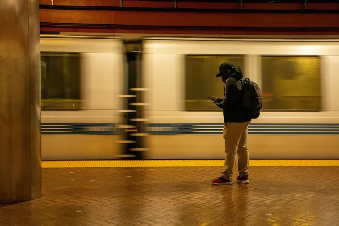 Dynamic urban scene of a commuter checking a phone while a train speeds past in a modern subway station.