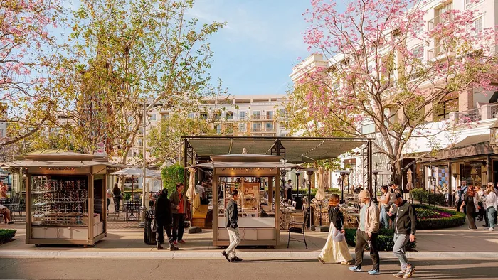 Vibrant urban scene showcasing a lively plaza with bustling outdoor cafes, modern architecture, and lush trees under a clear sky.