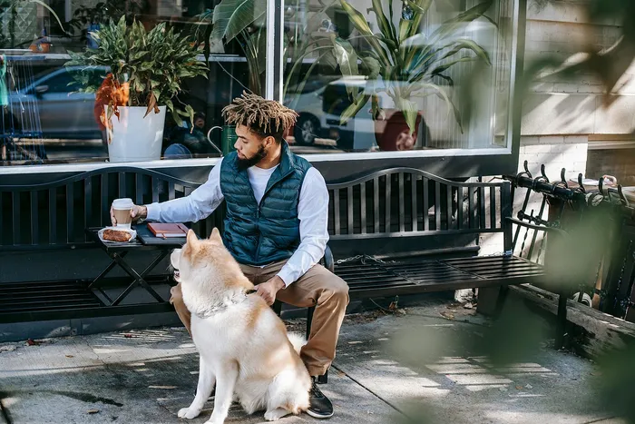 Relaxed urban scene with a stylish man enjoying coffee next to his loyal dog outside a charming cafe.
