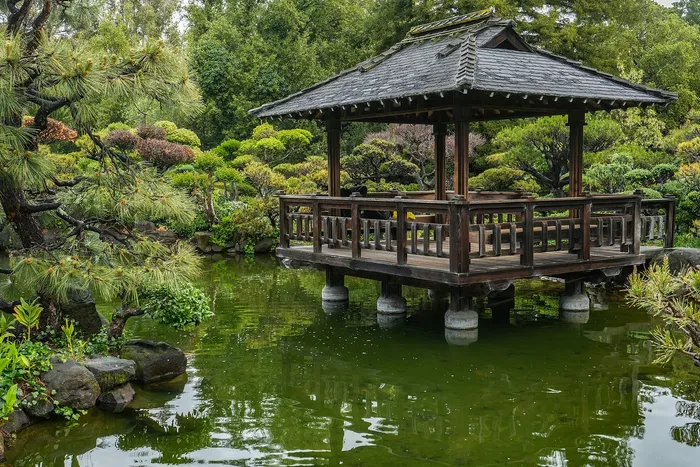 Serene Japanese garden featuring a charming wooden gazebo over a tranquil pond surrounded by lush greenery.