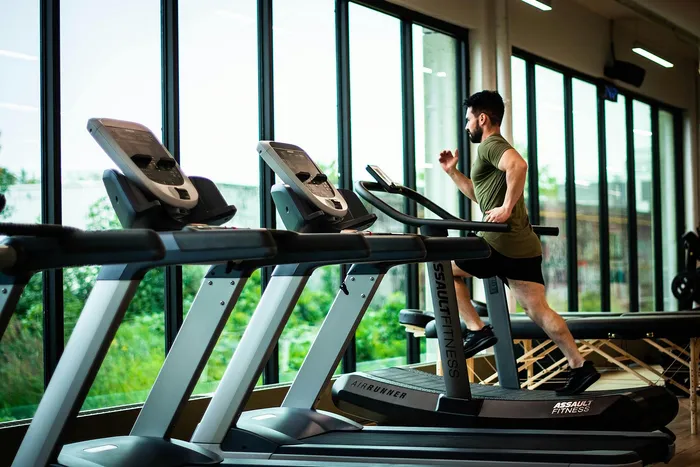 Modern gym with large windows offering natural light, featuring state-of-the-art treadmills in a vibrant fitness center.