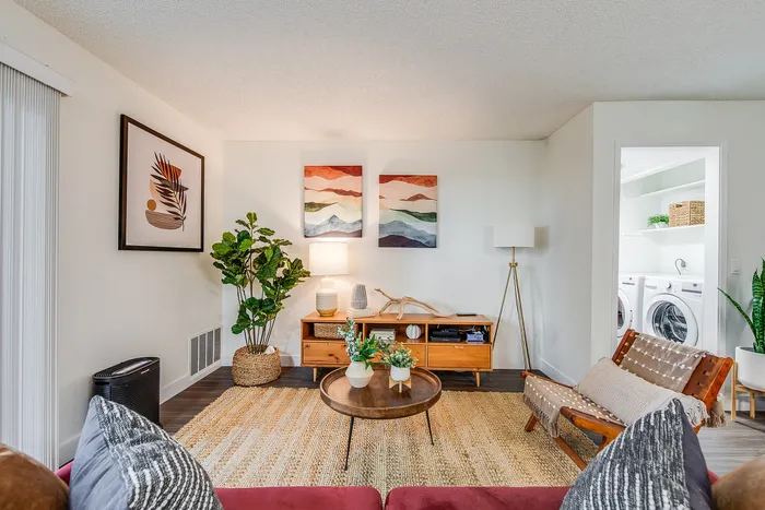 Inviting living room with stylish wooden furniture, vibrant art pieces, and lush greenery, leading into a convenient laundry area.