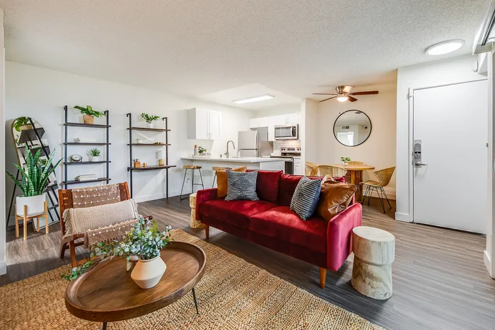 Modern open-concept living space with a cozy red sofa, stylish wood and metal shelving, elegant kitchen with stainless steel appliances, and a charming dining area with natural light.