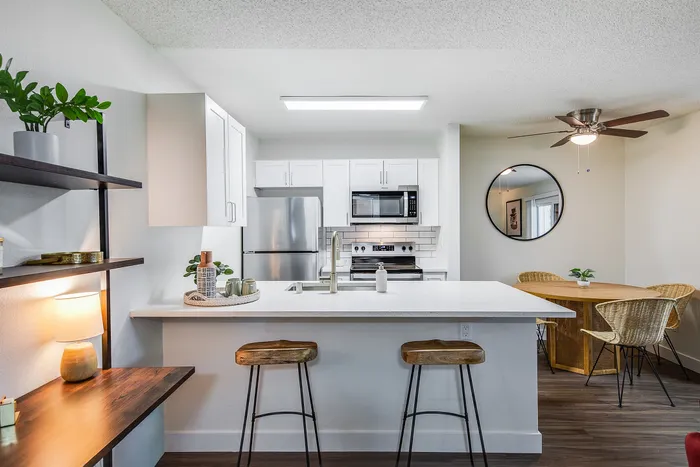 Chic apartment showcasing a modern kitchen with sleek white cabinetry, stylish stainless steel appliances, and a cozy dining area with elegant wicker chairs, perfect for culinary creativity and relaxation.
