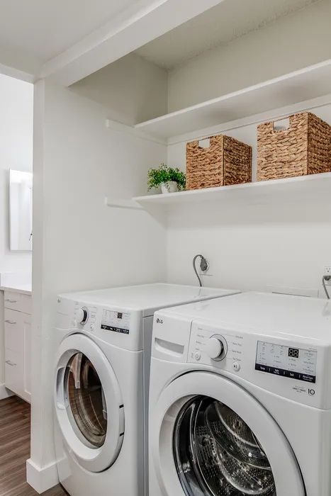 Modern laundry room with sleek white washer and dryer, featuring open shelving for stylish storage solutions and decor.