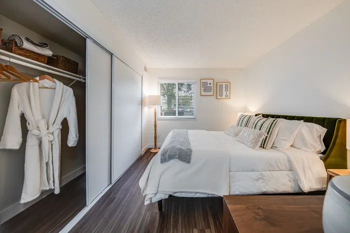 Elegant bedroom with plush bedding, wooden floors, and ample closet space, illuminated by natural light from a large window.
